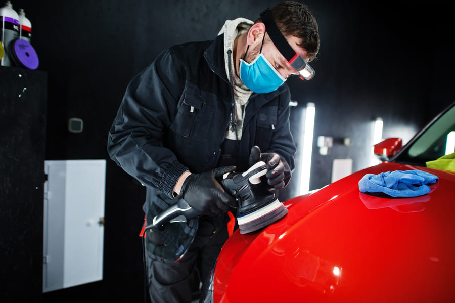 car-detailing-concept-man-face-mask-with-orbital-polisher-repair-shop-polishing-orange-suv-car blacharz samochodowy autoryzowany serwis
